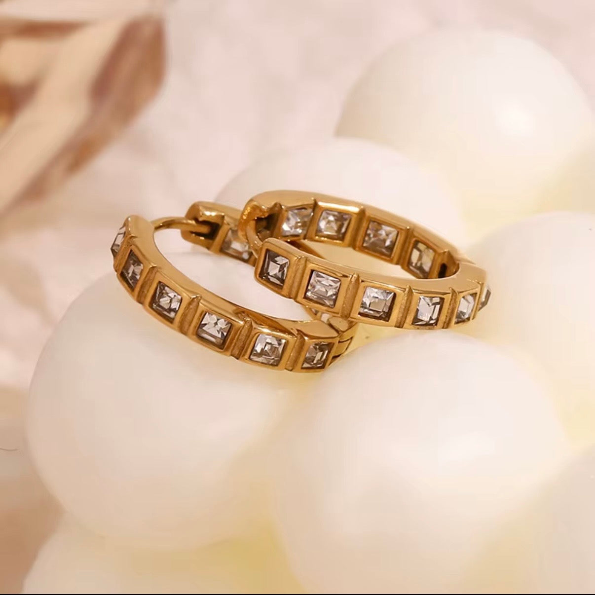18k gold channel-set emerald-cut CZ eternity huggie hoop earrings displayed on neutral stone surface — hypoallergenic water-resistant tarnish-resistant stackable everyday luxury huggies by The Intertwined Collective, Dallas Texas