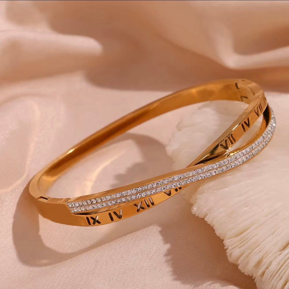 Gold hinged bangle bracelet with engraved Roman numerals and crossover pavé CZ crystal row shown on wet surface and on wrist – hypoallergenic water and tarnish resistant bracelet