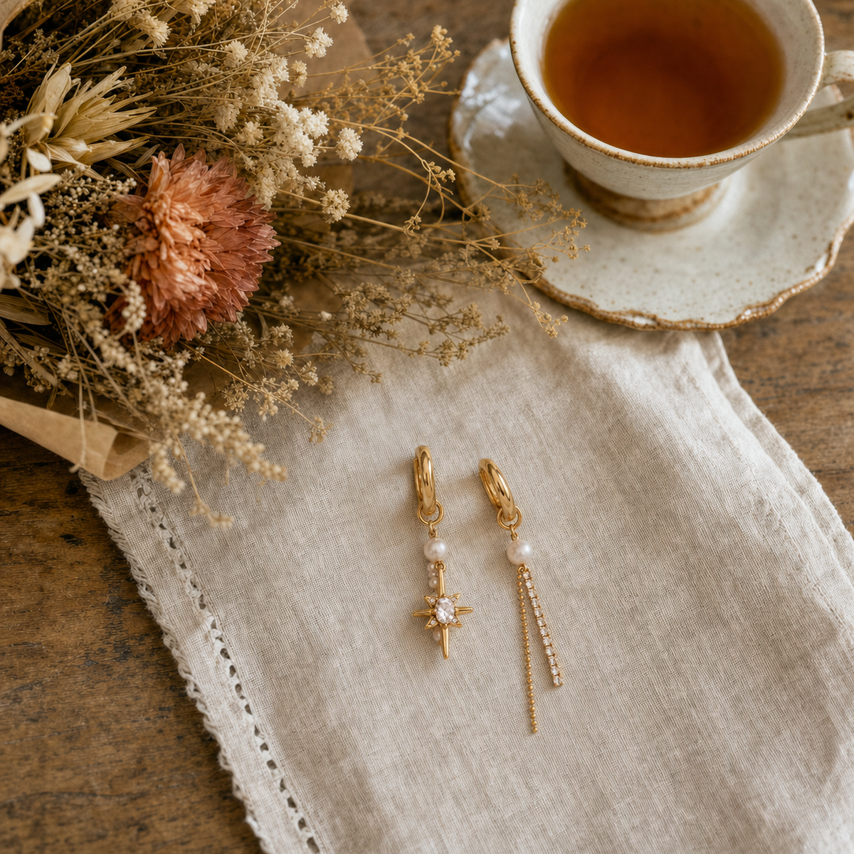 18k gold plated stainless steel mismatched huggie earrings with baroque pearl CZ north star charm and CZ tennis chain drop, hypoallergenic tarnish resistant editorial statement earrings by The Intertwined Collective, Dallas Texas — displayed on a linen napkin with tea and dried florals
