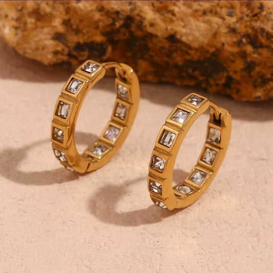 18k gold channel-set emerald-cut CZ eternity huggie hoop earrings displayed on neutral stone surface — hypoallergenic water-resistant tarnish-resistant stackable everyday luxury huggies by The Intertwined Collective, Dallas Texas