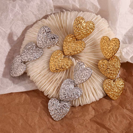 Gold and silver molten-texture double heart drop earrings displayed on dried botanical and kraft paper — 18k gold plated hypoallergenic water-resistant tarnish-resistant statement earrings by The Intertwined Collective, Dallas Texas