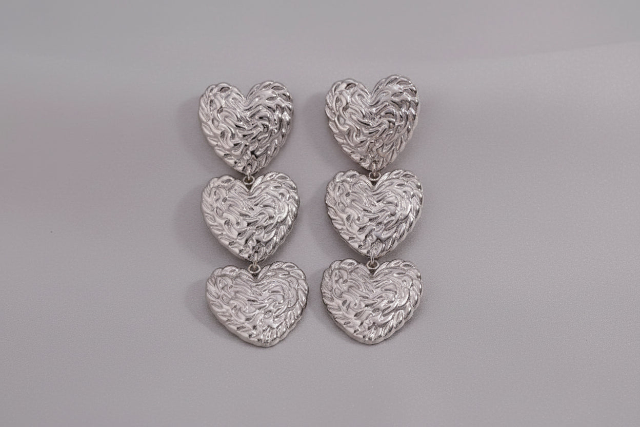 Silver molten-texture double heart drop earrings displayed on dried botanical and kraft paper — 18k gold plated hypoallergenic water-resistant tarnish-resistant statement earrings by The Intertwined Collective, Dallas Texas