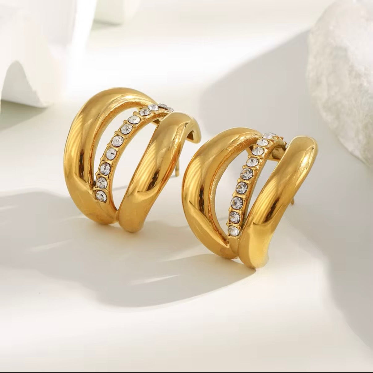 18k gold triple-band hoop earrings with CZ crystal center row displayed on white stone — hypoallergenic water-resistant tarnish-resistant chunky statement hoops by The Intertwined Collective, Dallas Texas