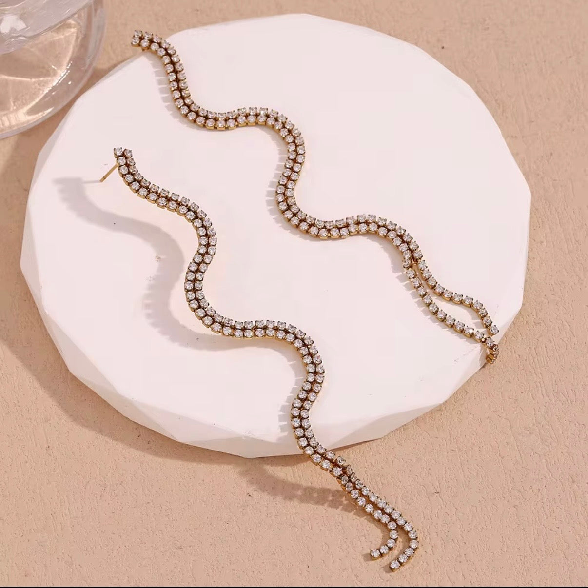 Gold double-row pavé CZ crystal wave fringe drop earrings displayed on neutral stone surface — hypoallergenic water-resistant tarnish-resistant long crystal statement earrings by The Intertwined Collective, Dallas Texas