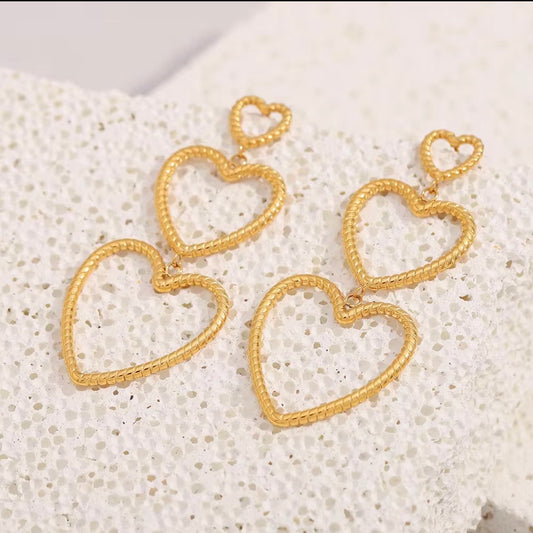 Gold triple heart drop earrings with textured rope-style open hearts displayed on white stone – lightweight hypoallergenic water- and tarnish‑resistant statement earrings