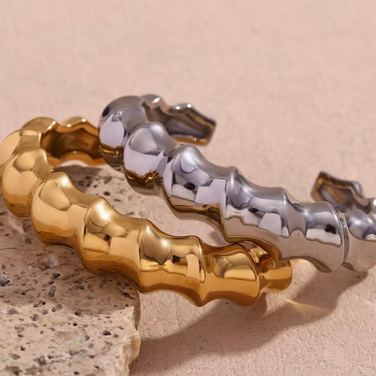 Chunky sculpted wave band bangle in high‑polish gold and silver displayed on stone and soft fabric – hypoallergenic water and tarnish resistant statement bangle