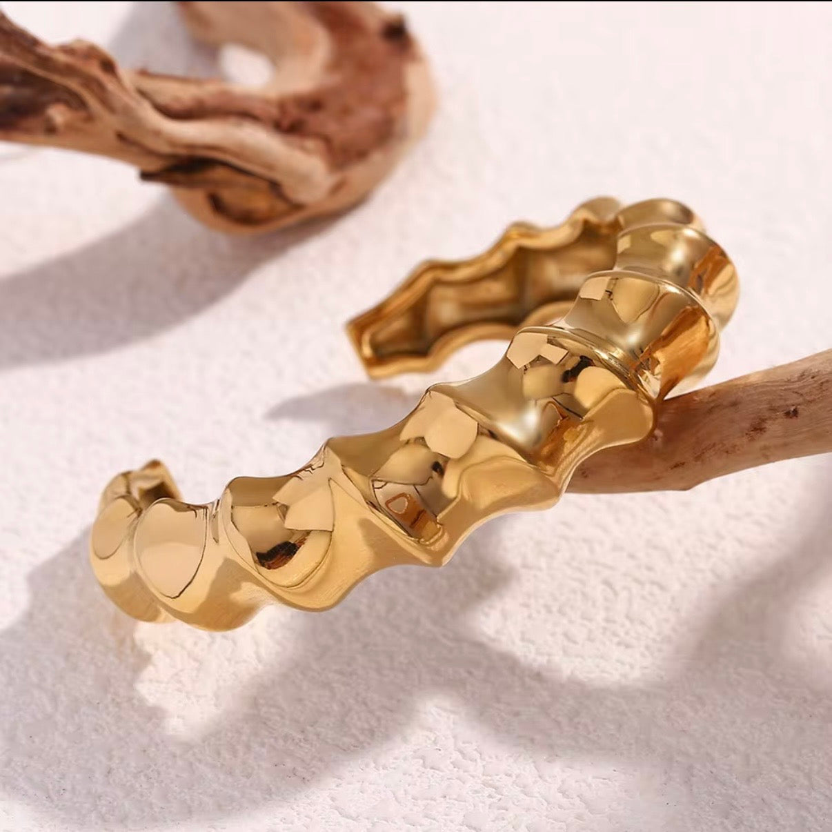 Chunky sculpted wave band bangle in high‑polish gold displayed on stone and soft fabric – hypoallergenic water and tarnish resistant statement bangle
