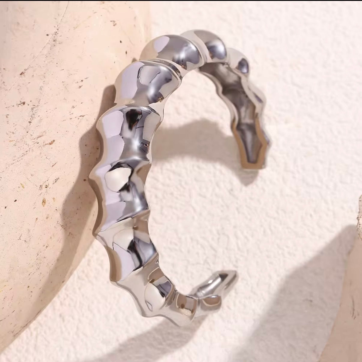 Chunky sculpted wave band bangle in high‑polish silver displayed on stone and soft fabric – hypoallergenic water and tarnish resistant statement bangle