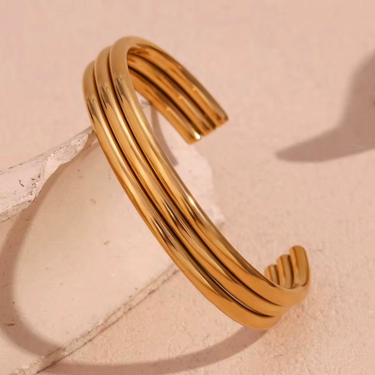 High‑polish gold open cuff bangle with triple parallel bands displayed on soft neutral surface – hypoallergenic water and tarnish resistant bracelet