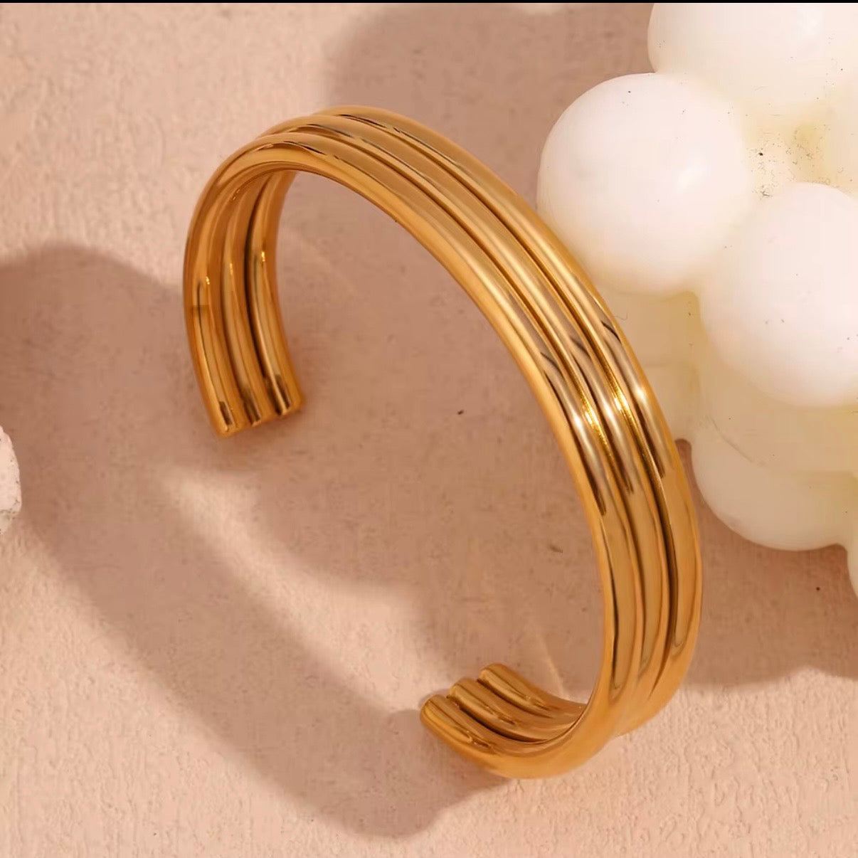 High‑polish gold open cuff bangle with triple parallel bands displayed on soft neutral surface – hypoallergenic water and tarnish resistant bracelet