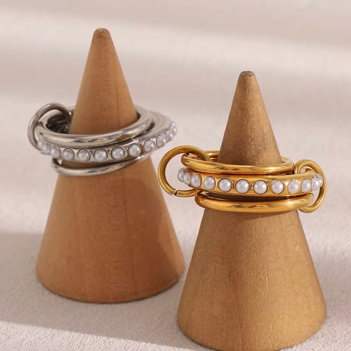 Gold and silver linked triple multi-band rings with center row of faux pearls displayed on wooden ring cones – hypoallergenic water and tarnish resistant pearl statement rings