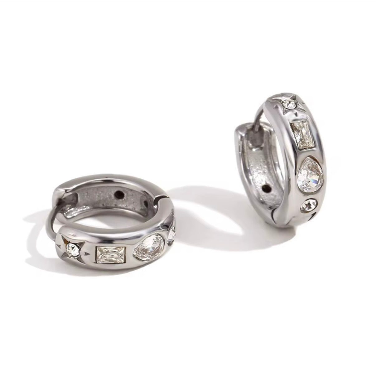 Chunky silver huggie hoop earrings with mixed pear, baguette, and round CZ stones and starburst detailing on marble surface – also available in gold, hypoallergenic water and tarnish resistant