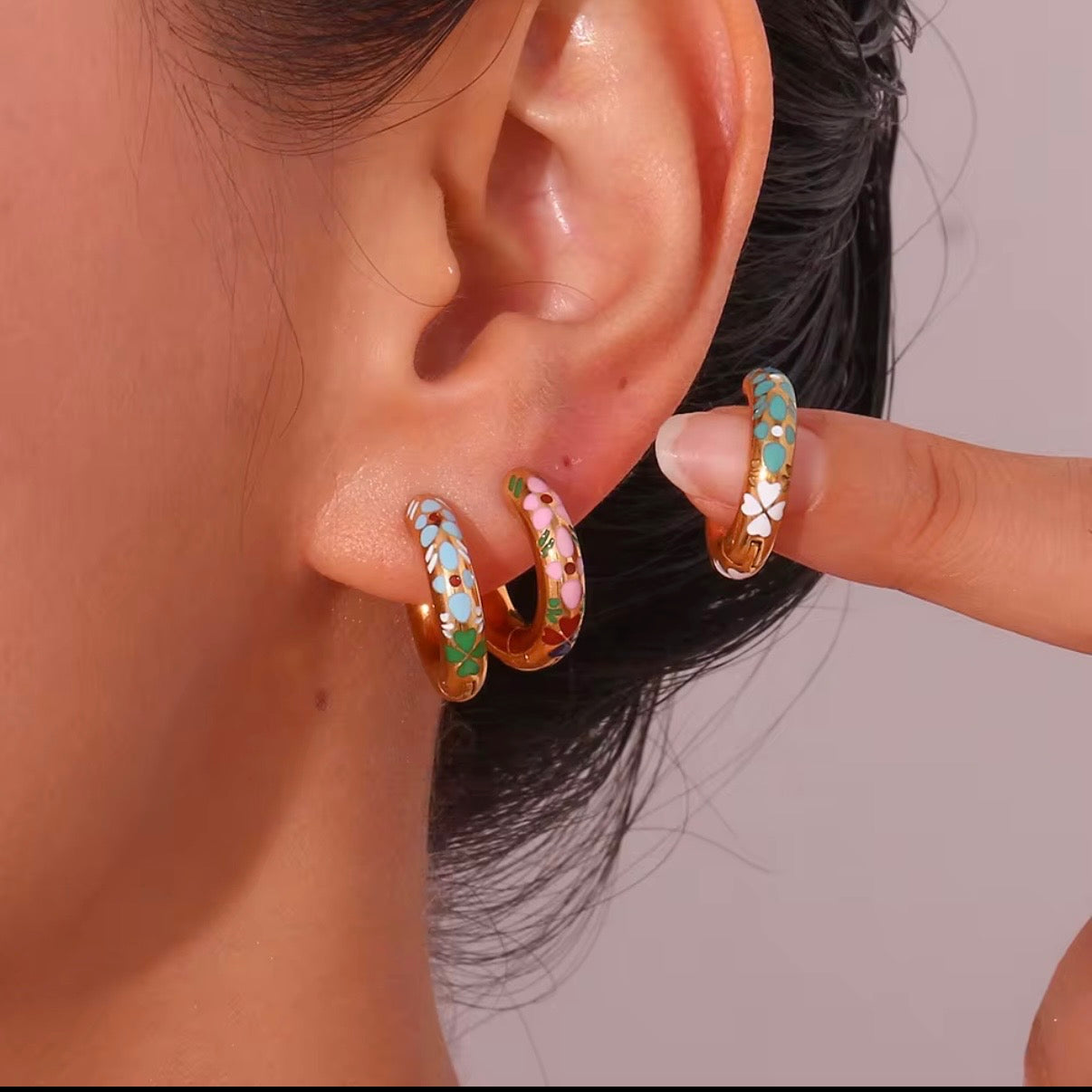 Three pairs of small gold huggie hoop earrings with colorful floral enamel in mint green, soft pink, and sky blue displayed on bar and stone – hypoallergenic water and tarnish resistant huggies