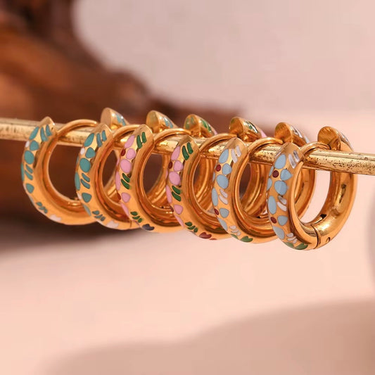 Three pairs of small gold huggie hoop earrings with colorful floral enamel in mint green, soft pink, and sky blue displayed on bar and stone – hypoallergenic water and tarnish resistant huggies