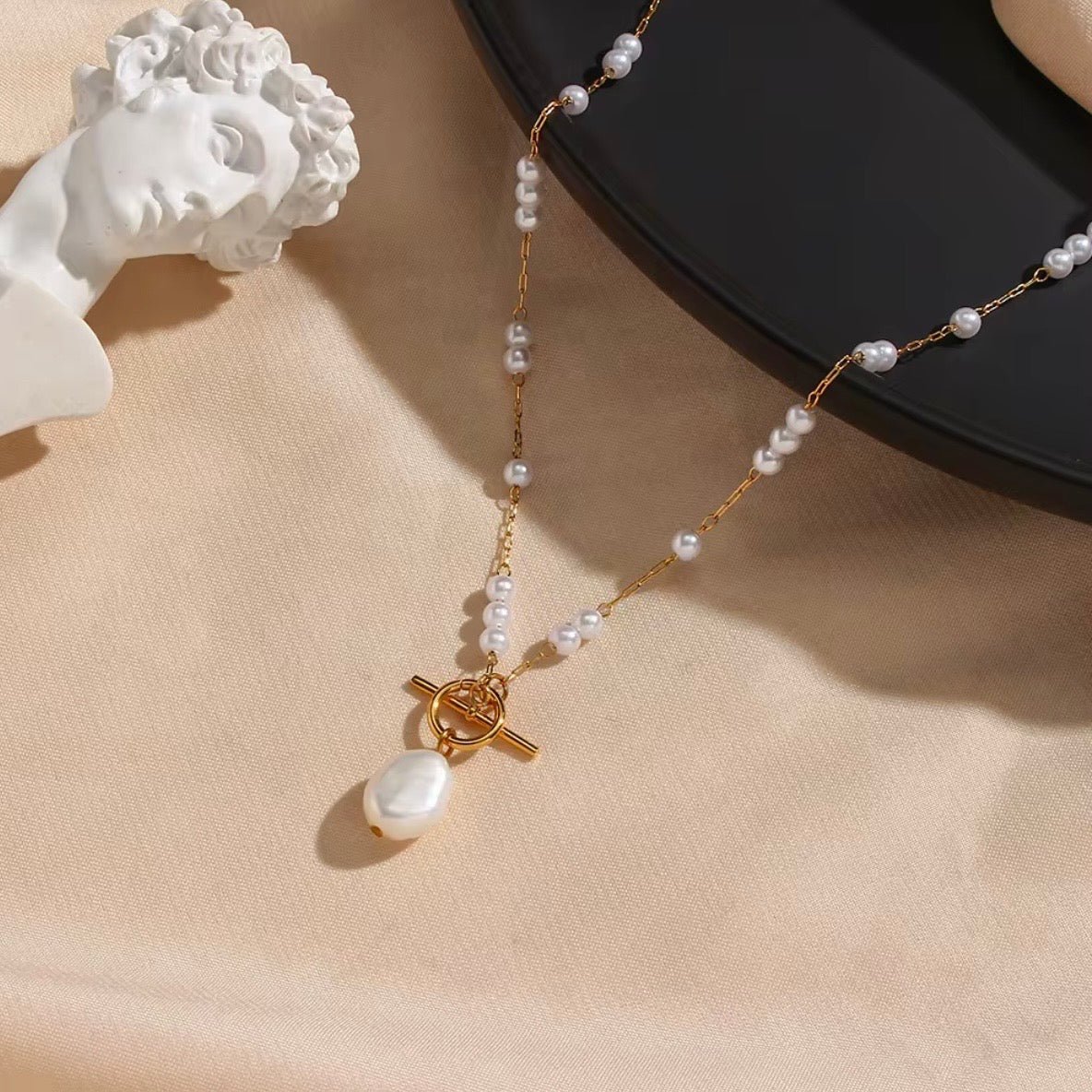 Layered gold necklaces on model wearing black sweater, featuring pearl station chain with drop pearl pendant and shorter gold oval medallion – hypoallergenic water and tarnish resistant layered necklace set