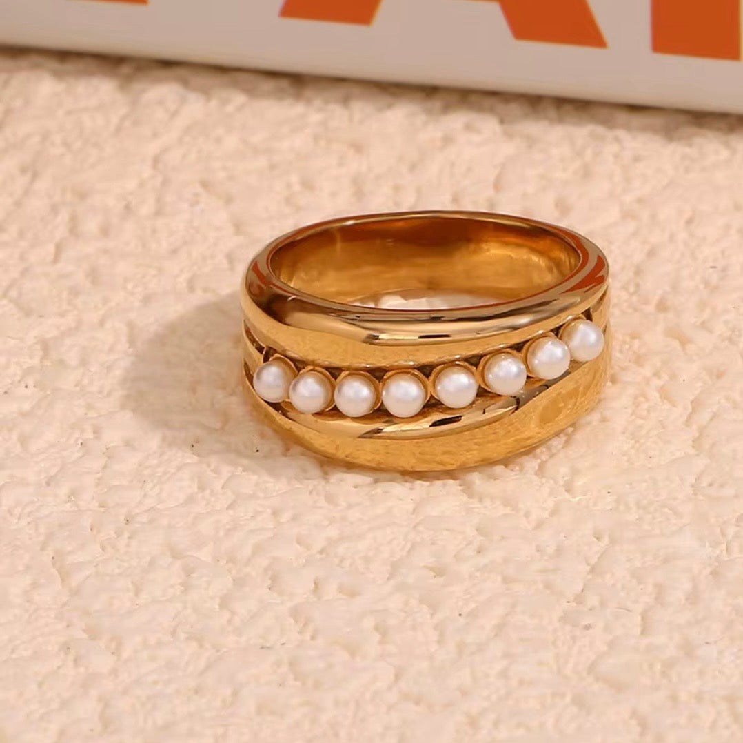 Wide gold wave band ring with center row of faux pearls displayed on textured cream surface – hypoallergenic water and tarnish resistant pearl statement ring