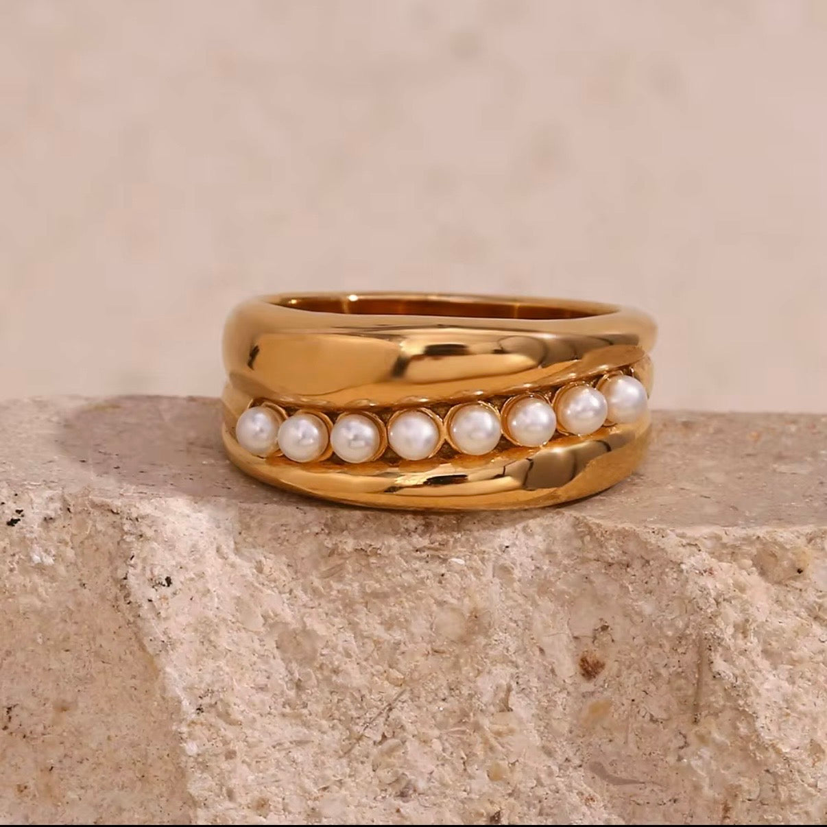 Wide gold wave band ring with center row of faux pearls displayed on textured cream surface – hypoallergenic water and tarnish resistant pearl statement ring