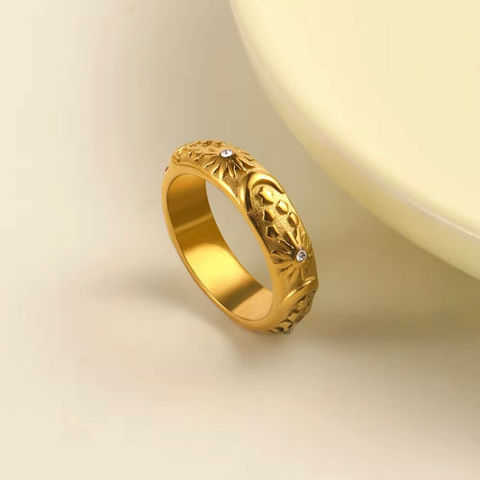 Gold matte celestial band ring with embossed sun, moon and star engravings and tiny CZ crystal accents on cream background – hypoallergenic water and tarnish resistant ring