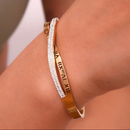 Gold hinged bangle bracelet with engraved Roman numerals and crossover pavé CZ crystal row shown on wet surface and on wrist – hypoallergenic water and tarnish resistant bracelet