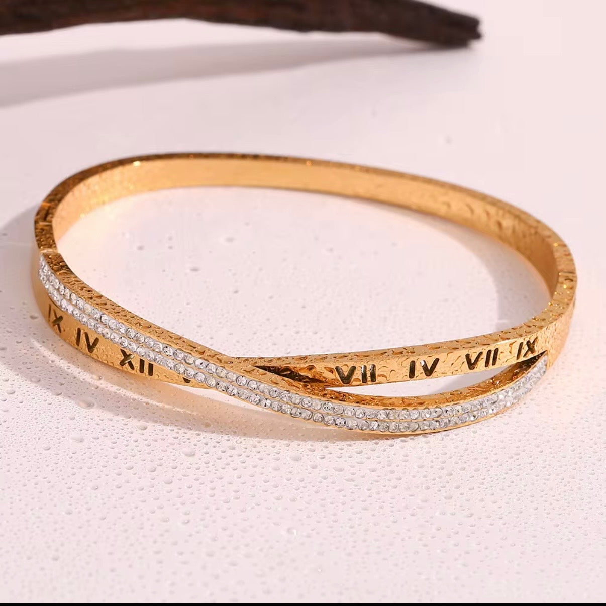 Gold hinged bangle bracelet with engraved Roman numerals and crossover pavé CZ crystal row shown on wet surface and on wrist – hypoallergenic water and tarnish resistant bracelet