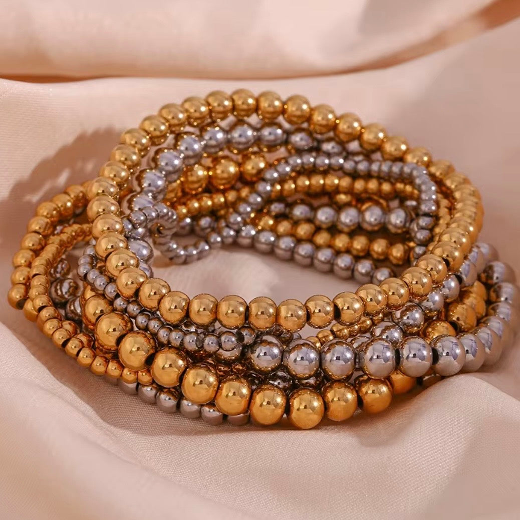 Gold and silver stretch bead bracelets in  3, 4, 5 and 6 mm sizes stacked together on soft fabric – hypoallergenic water and tarnish resistant beaded bracelets