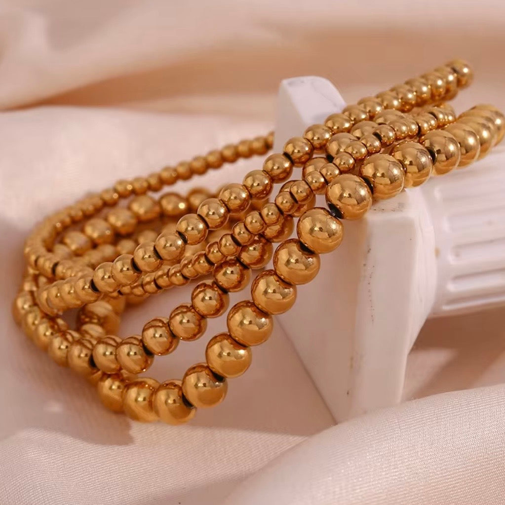 Gold stretch bead bracelets in  3, 4, 5 and 6 mm sizes stacked together on soft fabric – hypoallergenic water and tarnish resistant beaded bracelets