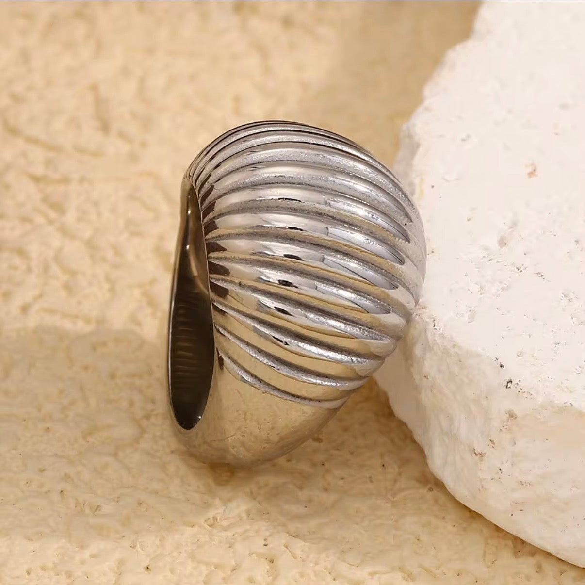 Silver ring with ribbed design on a textured beige surface