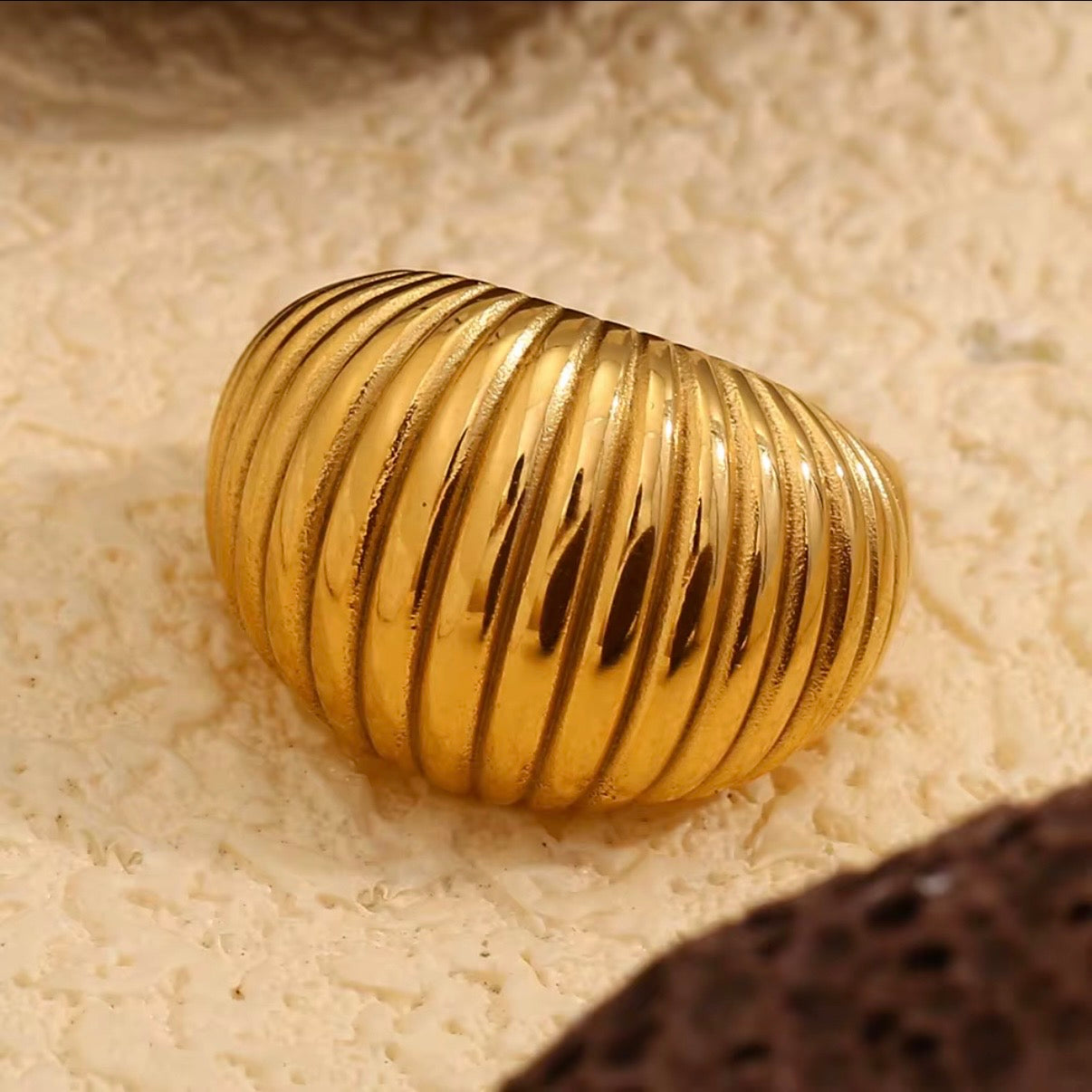 Gold ring with ribbed design on a textured beige surface