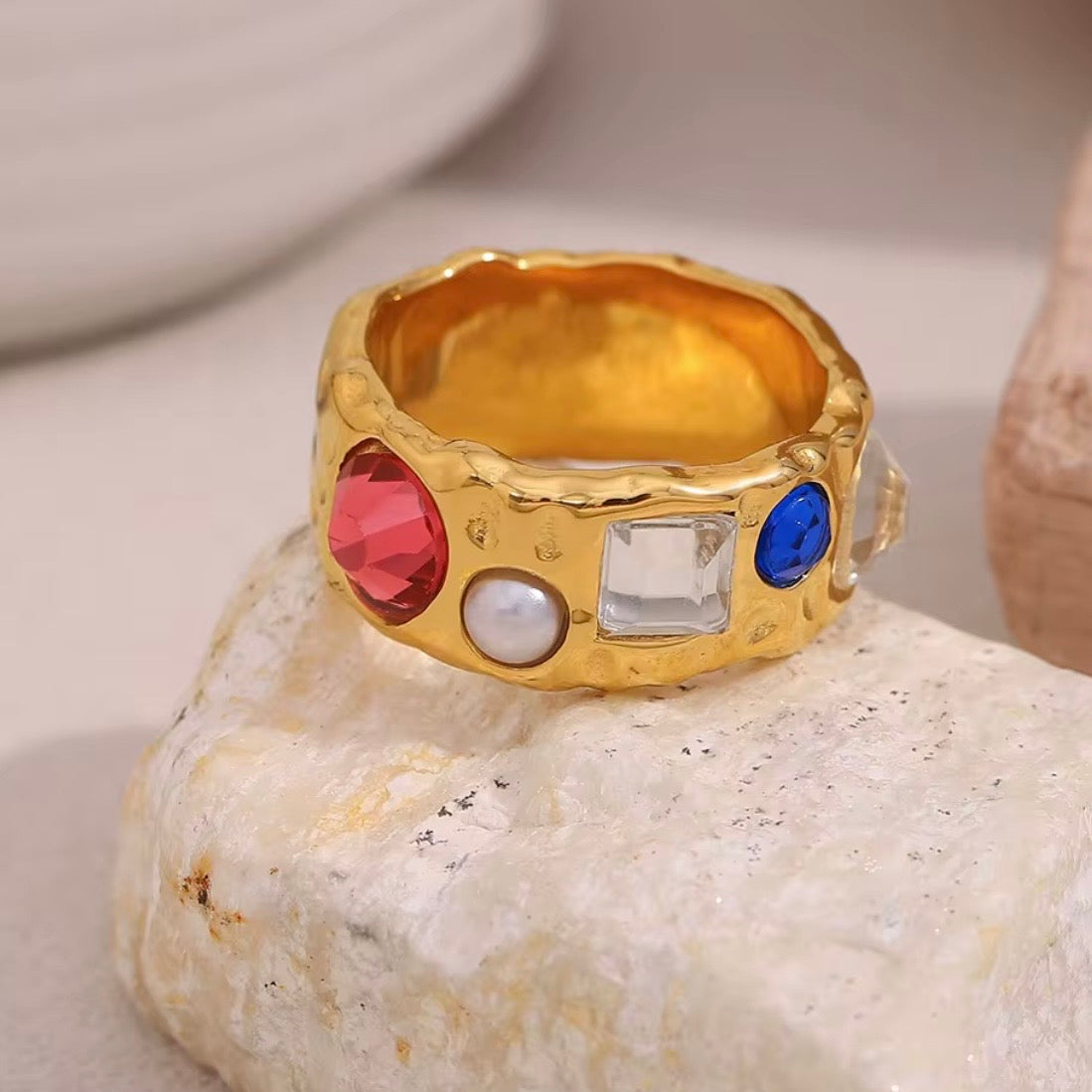 18k gold plated stainless steel wide hammered band ring with mixed scattered stones including red CZ, pearl, clear CZ, and blue CZ, maximalist vintage-inspired statement ring by The Intertwined Collective