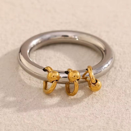 Two-tone stainless steel charm band ring with smooth silver tone band and three dangling 18k gold plated ball-and-hoop charms, hypoallergenic tarnish resistant playful statement ring by The Intertwined Collective
