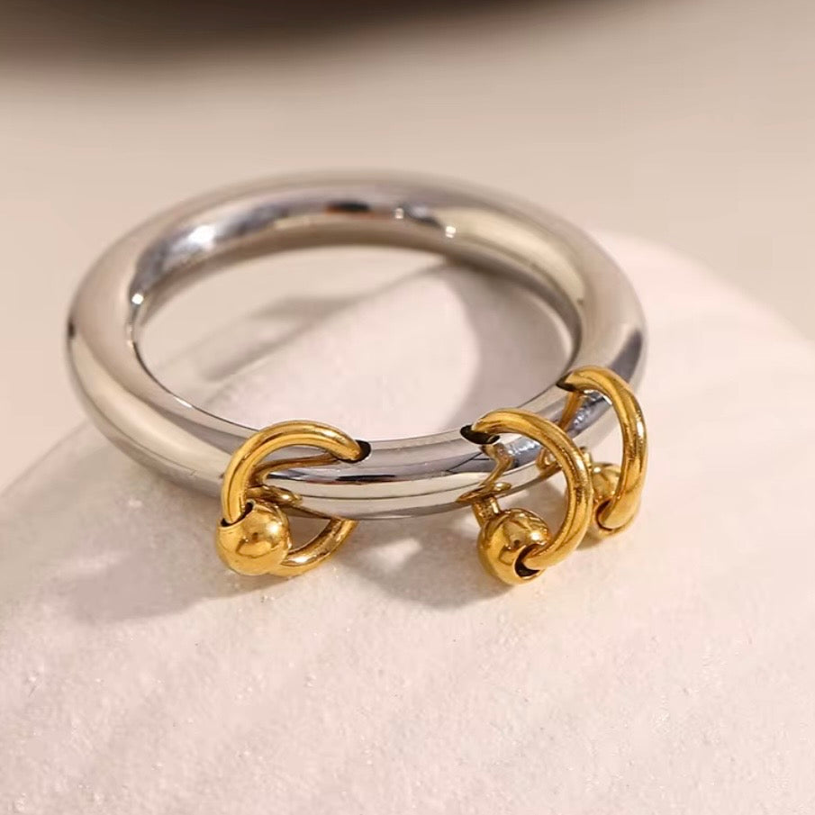 Two-tone stainless steel charm band ring with smooth silver tone band and three dangling 18k gold plated ball-and-hoop charms, hypoallergenic tarnish resistant playful statement ring by The Intertwined Collective