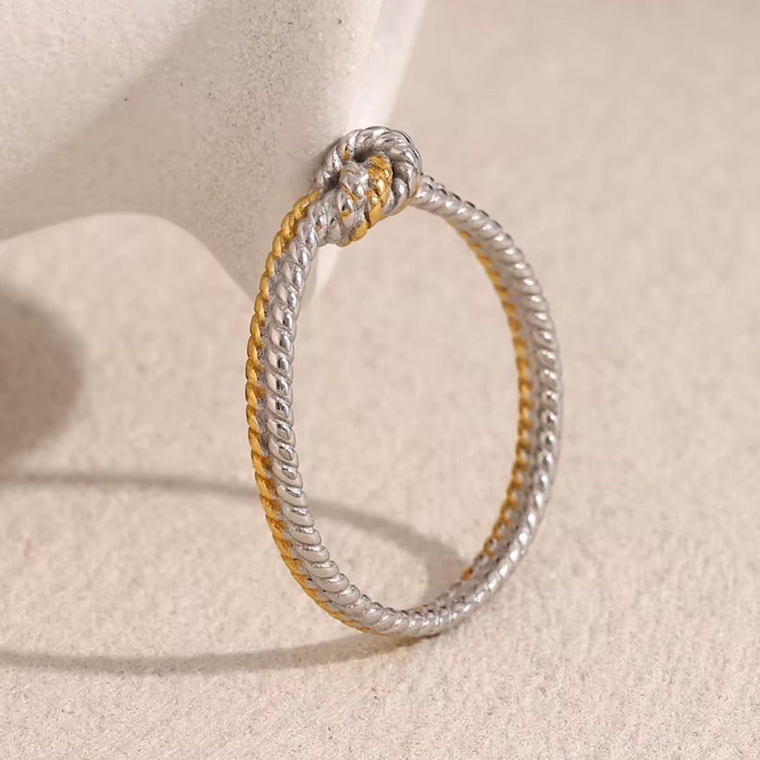 Two-tone stainless steel twisted rope knot ring with intertwined 18k gold plated and silver tone rope strands tied in a central knot, hypoallergenic tarnish resistant symbolic love ring by The Intertwined Collective
