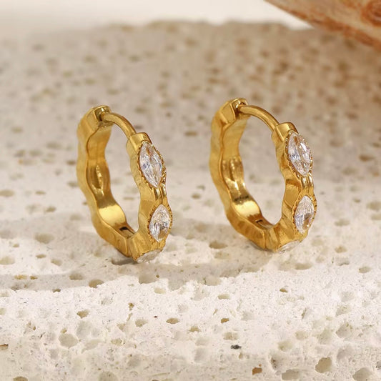 18k gold hammered huggie hoop earrings with two bezel-set marquise CZ stones displayed on neutral stone surface — hypoallergenic water-resistant tarnish-resistant stackable dainty huggie earrings by The Intertwined Collective, Dallas Texas