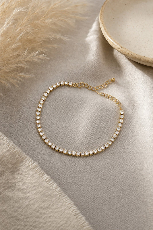 Gold tennis bracelet with clear CZ stones styled on linen with pampas grass