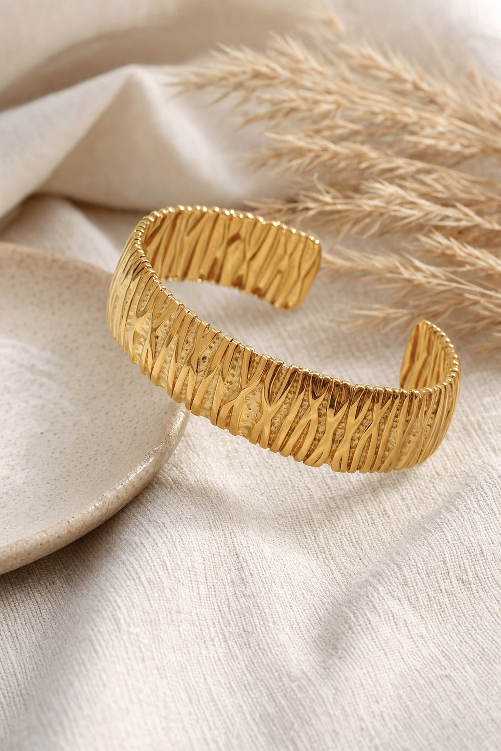 Gold textured open cuff bangle styled on linen with pampas grass